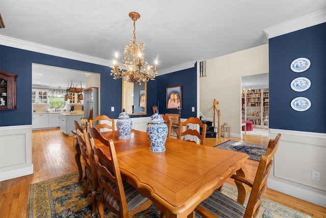dining space with an inviting chandelier, wainscoting, and light wood-type flooring