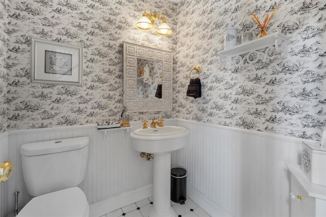 bathroom with tile patterned flooring, a wainscoted wall, toilet, and wallpapered walls