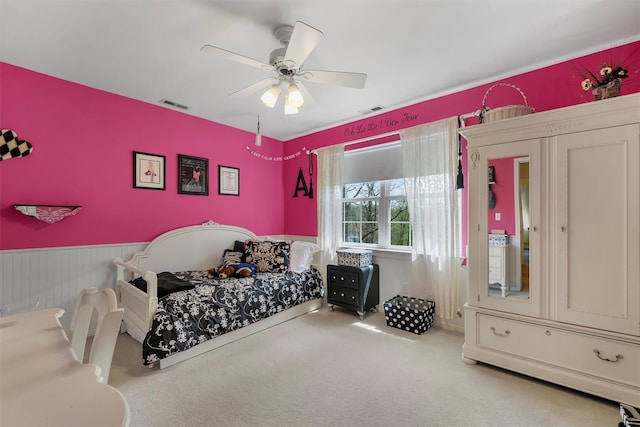 carpeted bedroom with a wainscoted wall, a ceiling fan, and visible vents