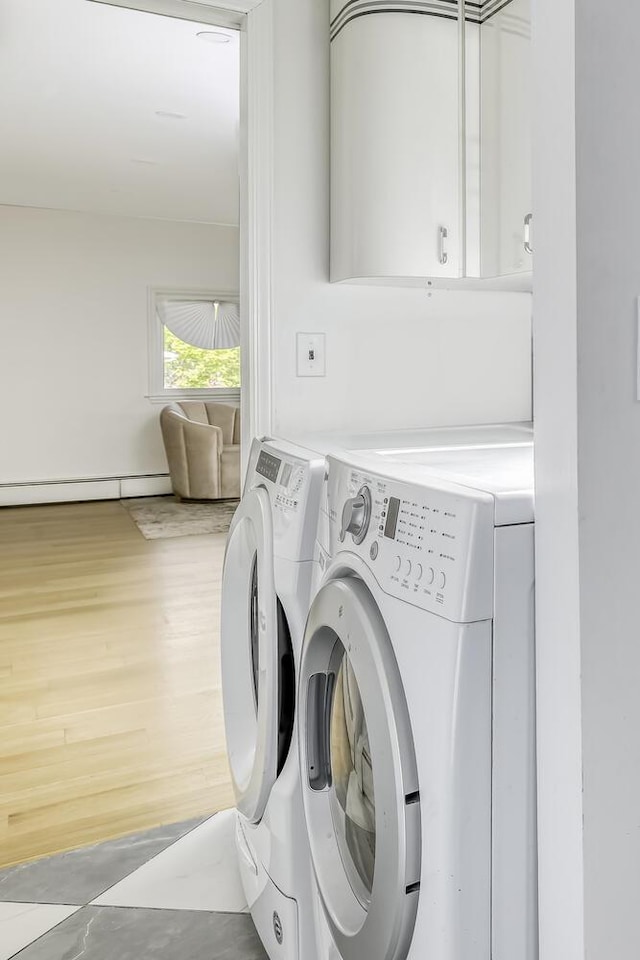clothes washing area with a baseboard heating unit, washing machine and dryer, and cabinet space