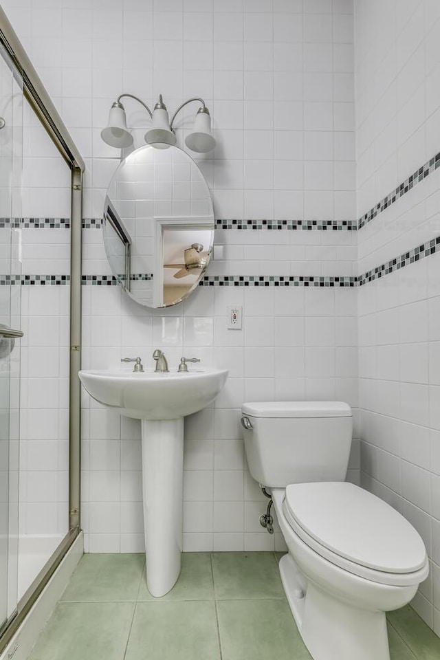 full bathroom featuring tile patterned flooring, tile walls, toilet, a sink, and a stall shower
