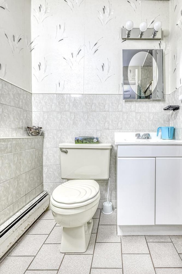 half bath featuring toilet, tile walls, baseboard heating, and vanity