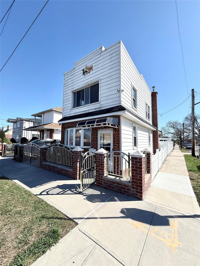 view of front of house with brick siding, a chimney, a fenced front yard, and a gate