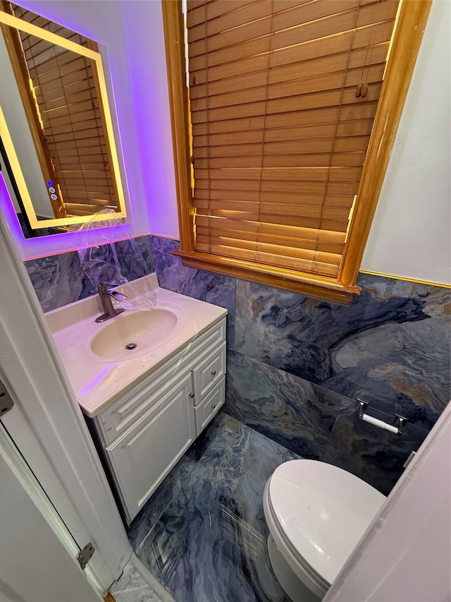 half bathroom featuring toilet, marble finish floor, tile walls, and vanity