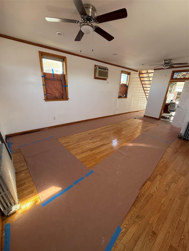 interior space with wood finished floors, ornamental molding, a ceiling fan, and a wall mounted AC