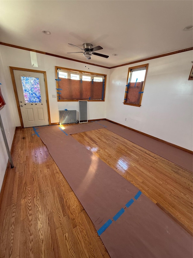 foyer featuring wood finished floors, a healthy amount of sunlight, radiator, ceiling fan, and ornamental molding