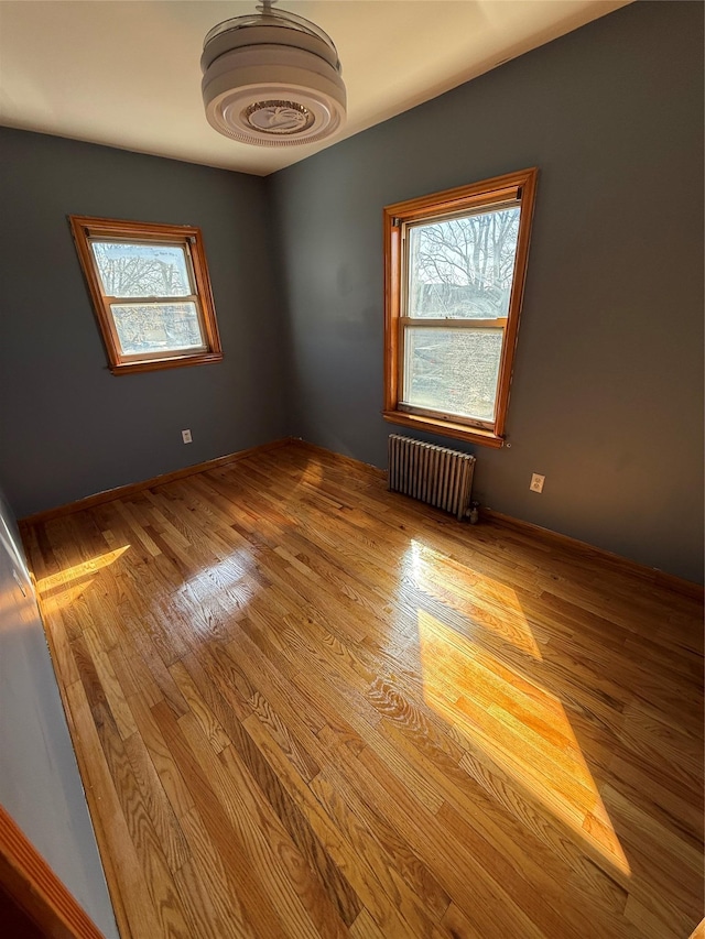 empty room with radiator heating unit, wood finished floors, and baseboards