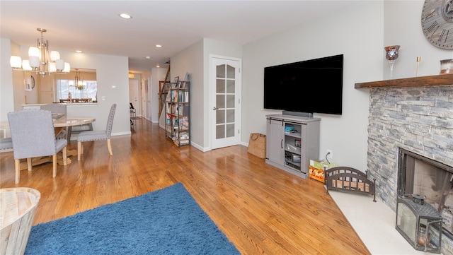 living area featuring recessed lighting, a chandelier, a stone fireplace, baseboards, and wood finished floors