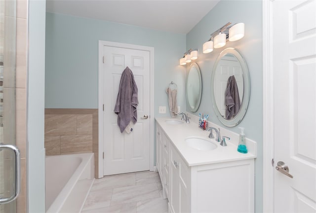 full bathroom featuring double vanity, a garden tub, marble finish floor, and a sink