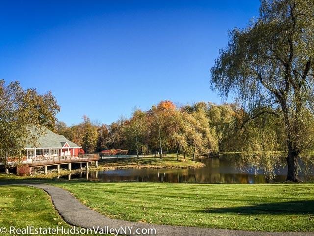 view of property's community with a wooded view, a deck with water view, and a lawn