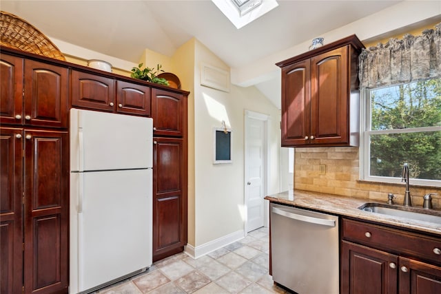 kitchen featuring backsplash, stainless steel dishwasher, a sink, freestanding refrigerator, and lofted ceiling with skylight