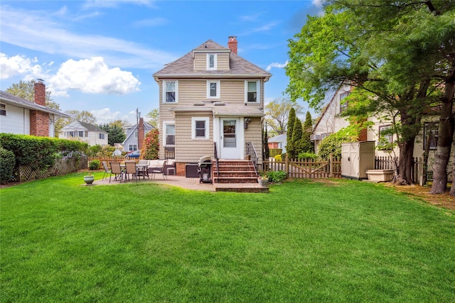 back of house with entry steps, a fenced backyard, a chimney, a patio area, and a yard