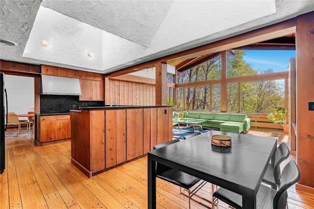 kitchen with exhaust hood, light wood finished floors, tasteful backsplash, brown cabinets, and vaulted ceiling