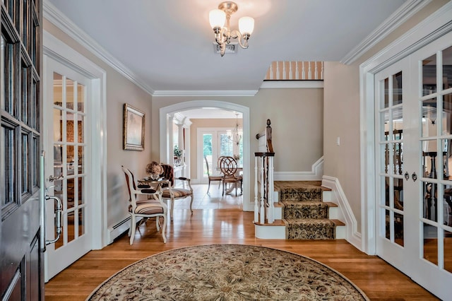 foyer entrance featuring an inviting chandelier, stairway, arched walkways, french doors, and wood finished floors