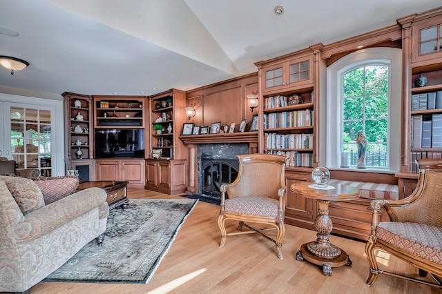 interior space featuring built in shelves, a fireplace with flush hearth, light wood-style flooring, and vaulted ceiling