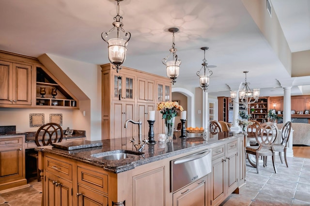 kitchen with a kitchen island with sink, dark stone counters, a warming drawer, a sink, and a notable chandelier