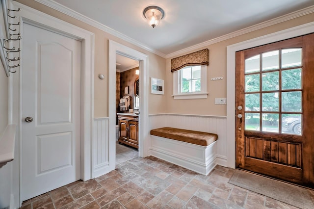entryway with crown molding, a wainscoted wall, and stone tile floors