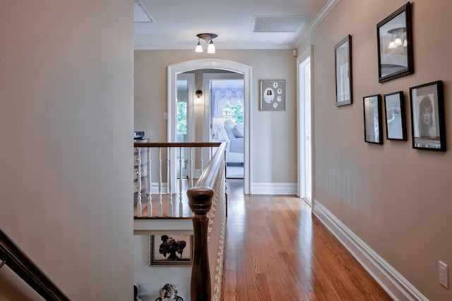 hallway featuring crown molding, light wood-style flooring, an upstairs landing, visible vents, and baseboards