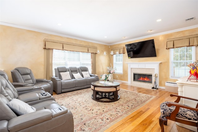 living area with visible vents, wood finished floors, a healthy amount of sunlight, and a premium fireplace