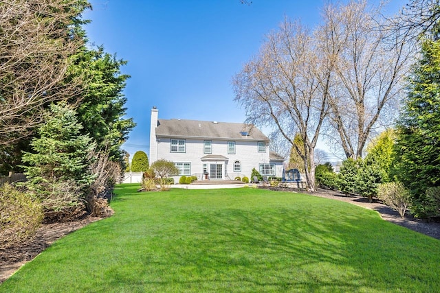 back of house featuring a lawn, a patio area, and a chimney