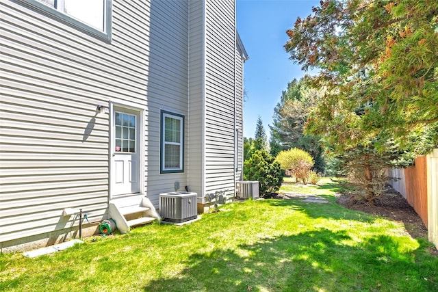 view of side of property featuring a lawn, central air condition unit, entry steps, and fence