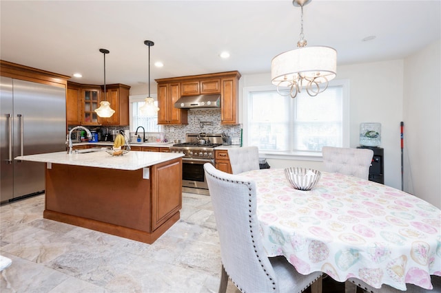 258 Longstreet Ave, Bronx, NY 10465 - kitchen featuring brown cabinets, under cabinet range hood, high end appliances, tasteful backsplash, and an island with sink