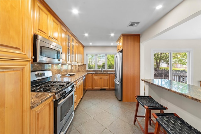 kitchen featuring appliances with stainless steel finishes, stone countertops, backsplash, glass insert cabinets, and a kitchen breakfast bar