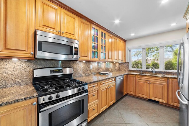 kitchen featuring stainless steel appliances, a sink, backsplash, dark stone countertops, and recessed lighting