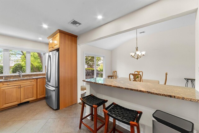 kitchen with freestanding refrigerator, a sink, a breakfast bar, dark stone countertops, and lofted ceiling