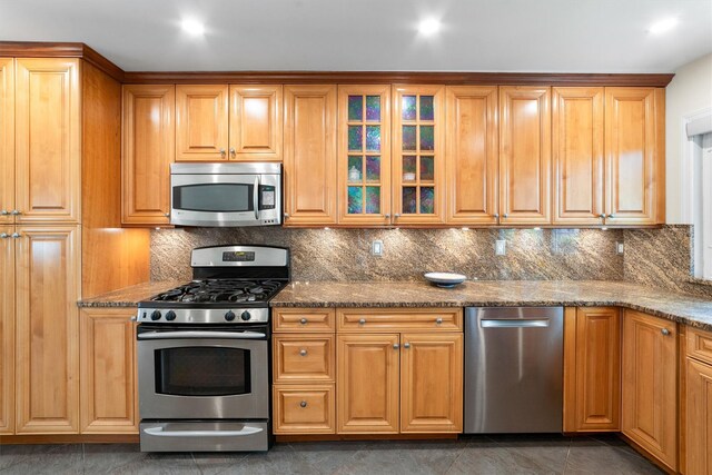 kitchen featuring stainless steel appliances, tasteful backsplash, dark stone countertops, and glass insert cabinets