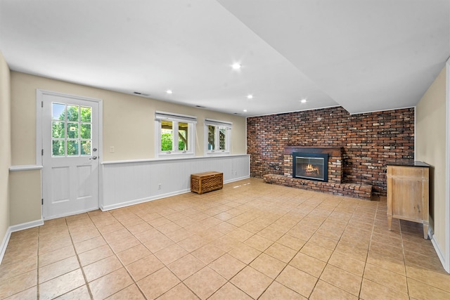 unfurnished living room featuring a brick fireplace, light tile patterned flooring, a wainscoted wall, brick wall, and recessed lighting
