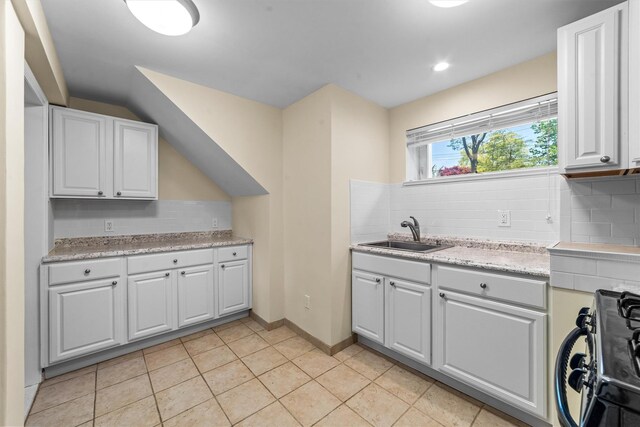 kitchen featuring a sink, black gas range, decorative backsplash, light tile patterned floors, and white cabinets