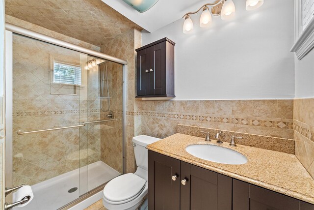 bathroom featuring tile walls, toilet, a stall shower, and vanity