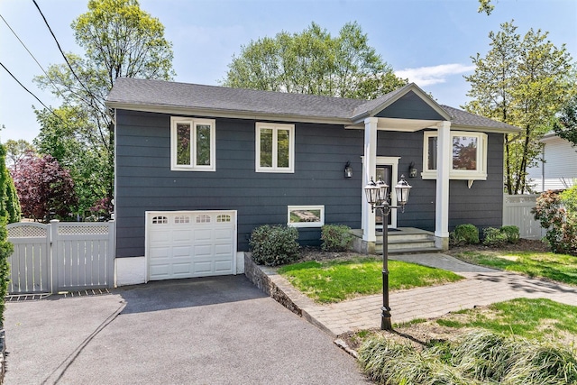 bi-level home with fence, a garage, and asphalt driveway