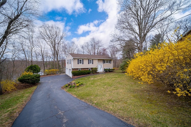 raised ranch featuring an attached garage, driveway, and a front yard