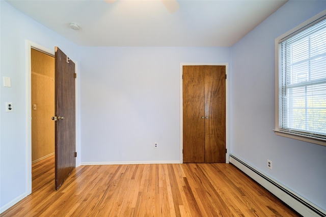 empty room with baseboards, a baseboard radiator, light wood-style flooring, and a wealth of natural light