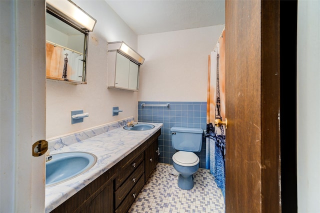 bathroom with a sink, wainscoting, toilet, and tile walls