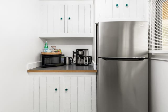kitchen with black microwave, freestanding refrigerator, and white cabinetry