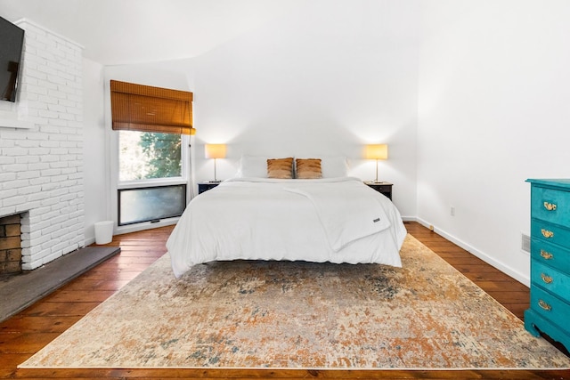 bedroom featuring hardwood / wood-style floors, baseboards, vaulted ceiling, and a brick fireplace
