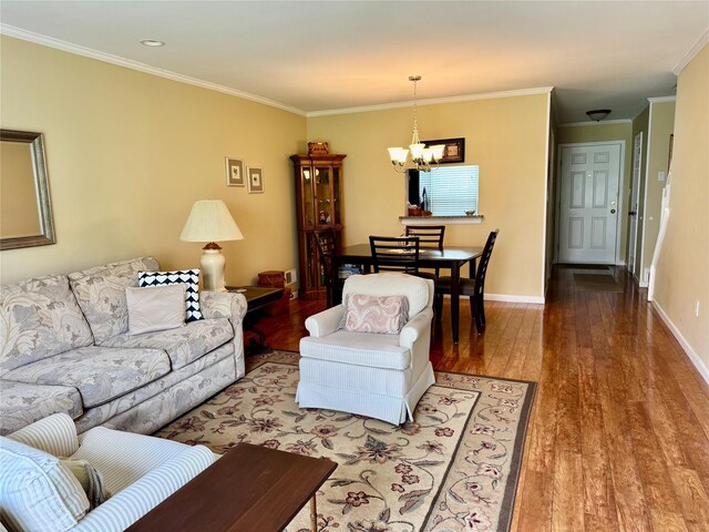 living area with baseboards, ornamental molding, a notable chandelier, and wood finished floors