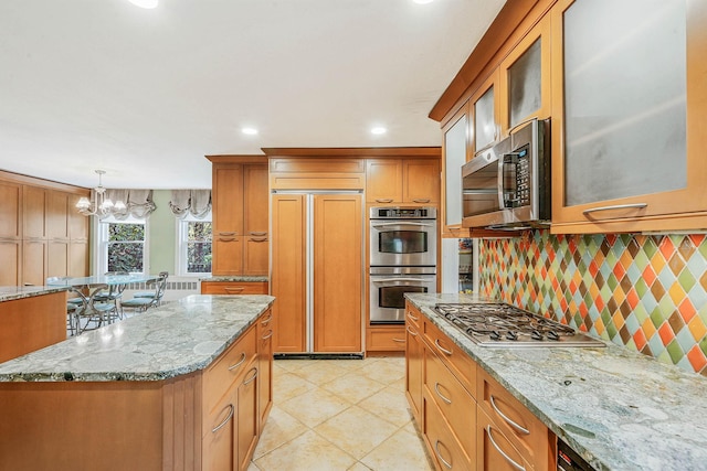 kitchen with light stone countertops, glass insert cabinets, decorative backsplash, a chandelier, and stainless steel appliances