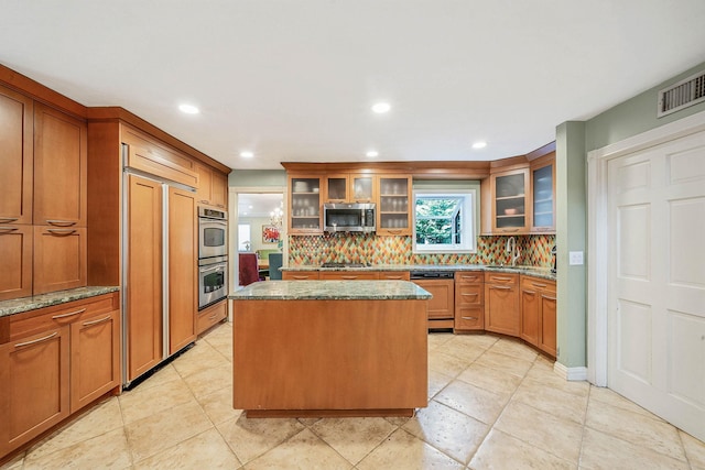 kitchen with a sink, paneled appliances, a center island, stone counters, and backsplash