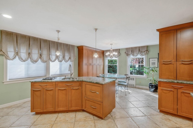 kitchen with light stone counters, a sink, baseboards, decorative light fixtures, and brown cabinetry