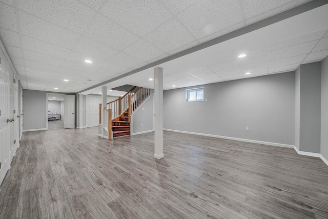 below grade area featuring recessed lighting, wood finished floors, a drop ceiling, baseboards, and stairway