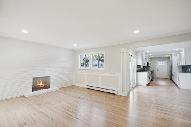 unfurnished living room with a sink, light wood-style flooring, a baseboard heating unit, and a fireplace