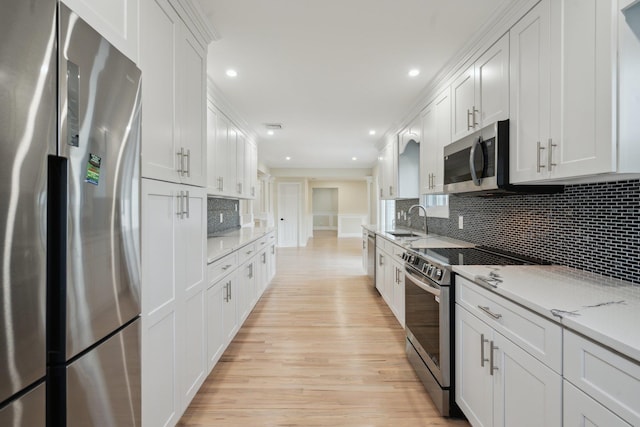 kitchen with appliances with stainless steel finishes, a sink, light wood finished floors, white cabinetry, and recessed lighting