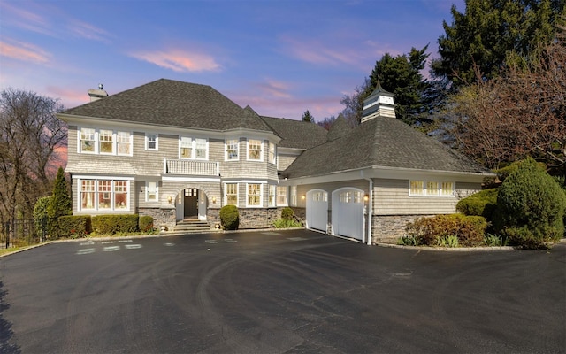 view of front of home featuring a chimney, roof with shingles, aphalt driveway, and stone siding
