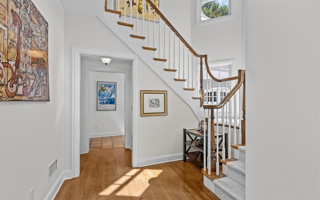 staircase with a high ceiling, visible vents, wood finished floors, and baseboards