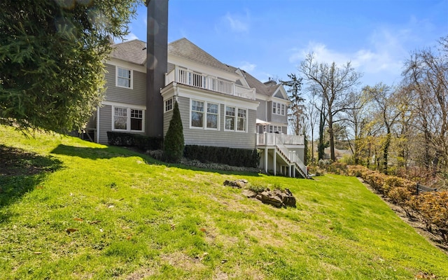 back of house with a lawn, roof with shingles, stairway, and a balcony