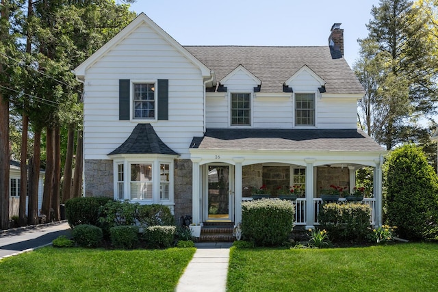 view of front of home featuring a porch, a chimney, stone siding, and a front lawn